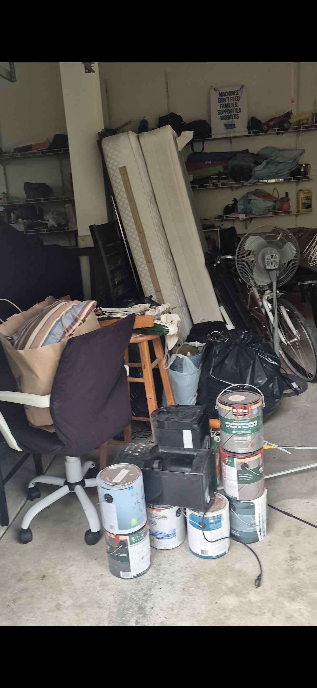 Cluttered garage in Easton, PA packed with mattresses, an office chair, paint cans, and bags before cleanout