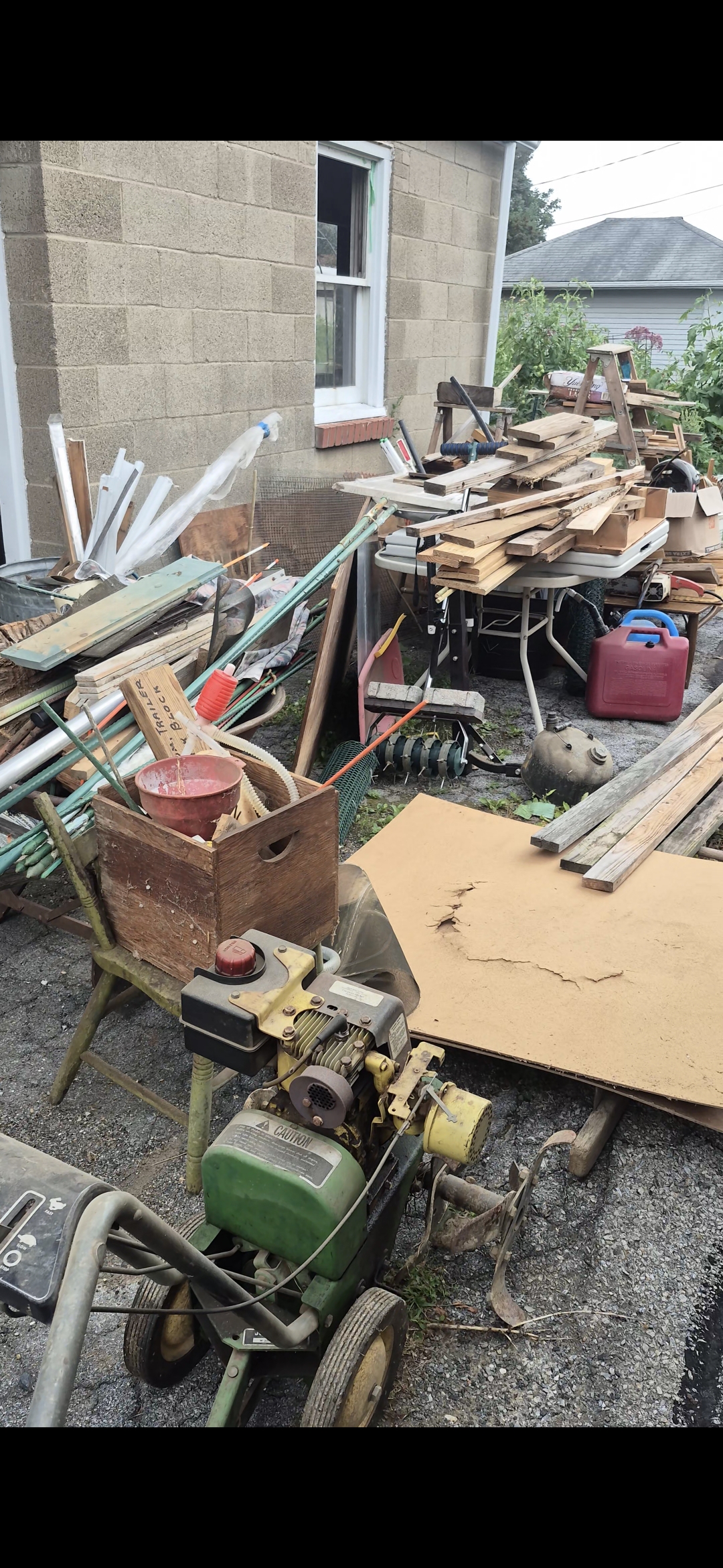 Backyard in Nazareth, PA cluttered with scrap lumber, a tiller, boxes, and gas cans before cleanout