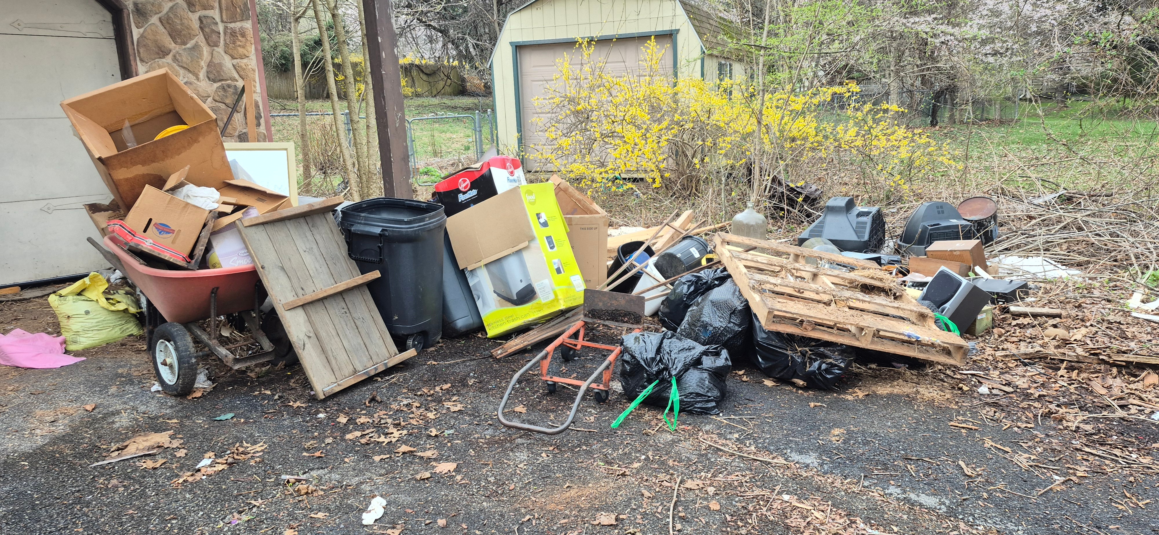 Curbside pile of junk in Emmaus, PA with a wheelbarrow, trash cans, boxes, bags, and a pallet before cleanout
